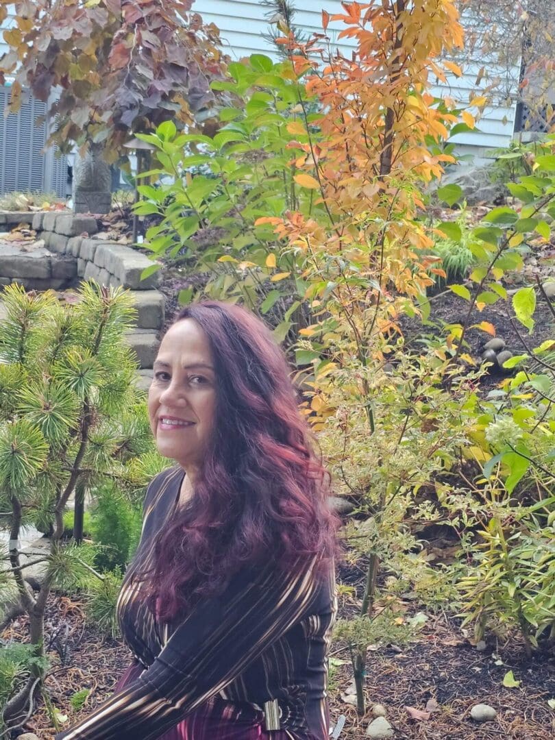 A woman with long hair stands outdoors amidst colorful autumn foliage.