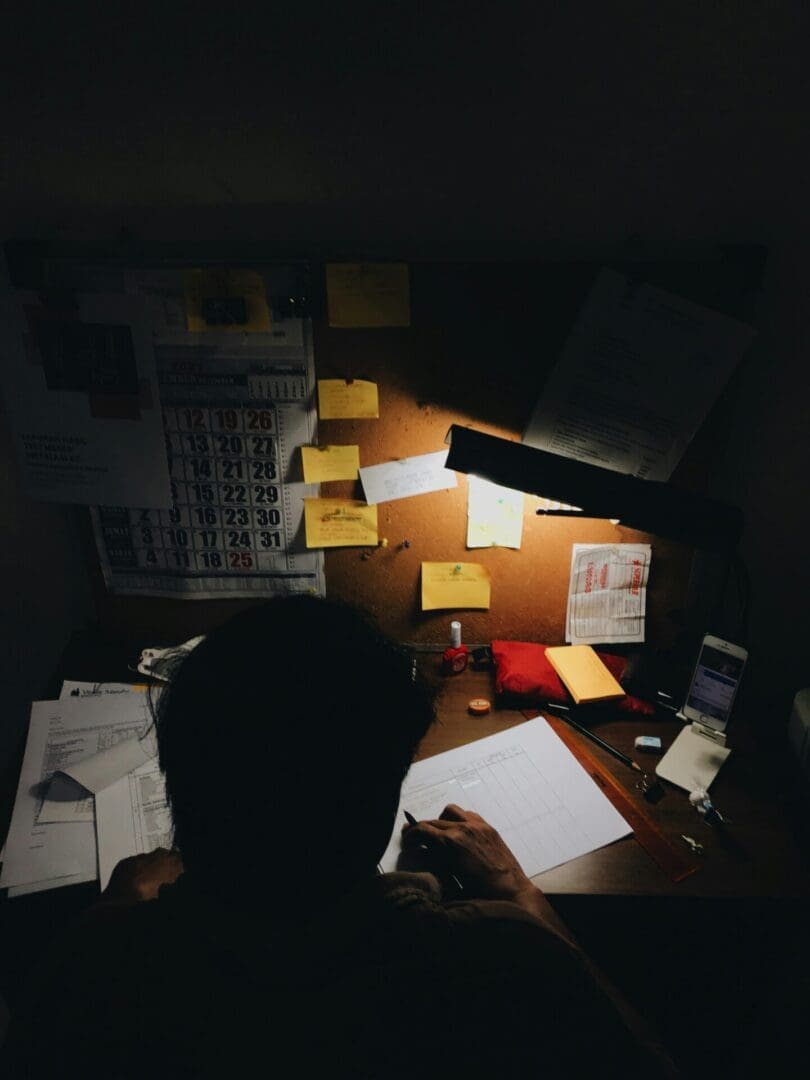Professional working late at a desk under a lamp, capturing the exhaustion and overwhelm often associated with burnout.