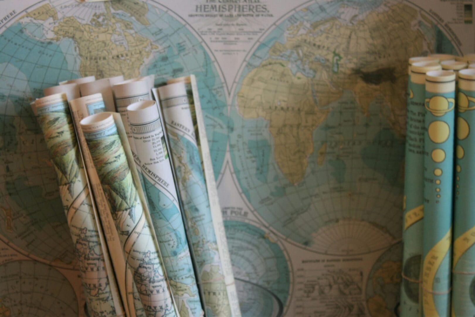 Rolled maps displayed in front of a world atlas, symbolizing perspective and discovery through virtual emotion-focused therapy in Washington state.